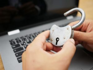 Hände halten ein Schloss, Laptop im Hintergrund verdeutlicht digitale Datensicherheit